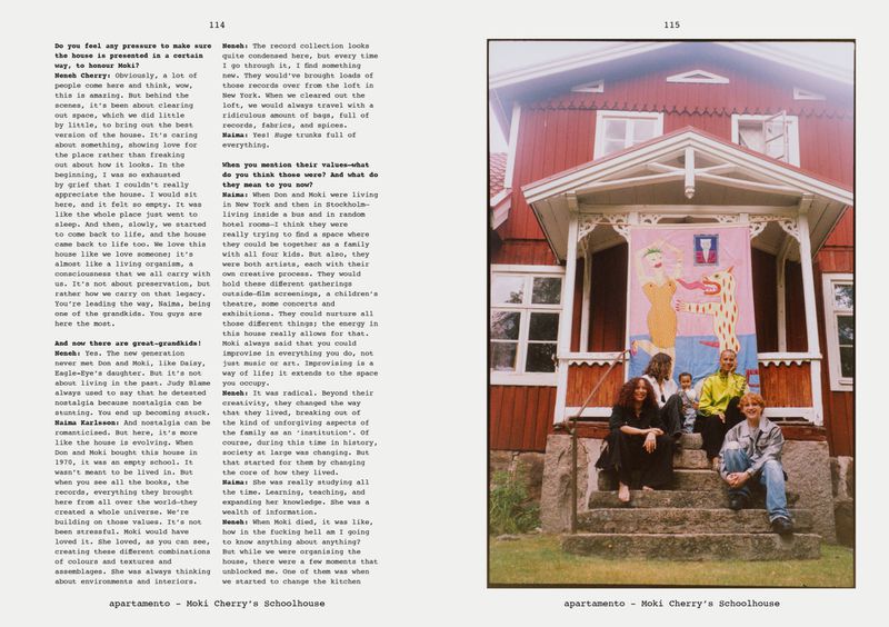 A group of people sits on the steps of a red house with a banner hanging above them, evoking a sense of community and artistic expression.