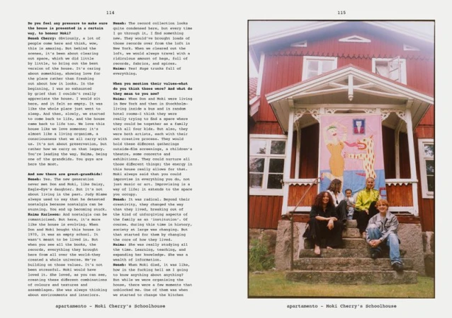 A group of people sits on the steps of a red house with a banner hanging above them, evoking a sense of community and artistic expression.