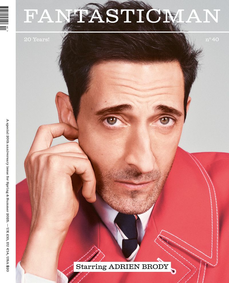 Magazine cover featuring headshot of Adrien Brody wearing a red coat and tie, looking at the camera against a neutral grey background.