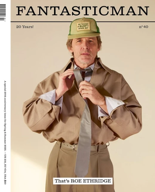 Fantastic Man magazine cover featuring a man in a tan trench coat and baseball cap, adjusting his tie against a beige background.