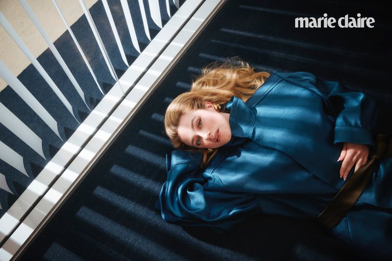 Blonde woman in blue coat lies on blue carpet with white accents, shot from above with a focus on fashion and style.