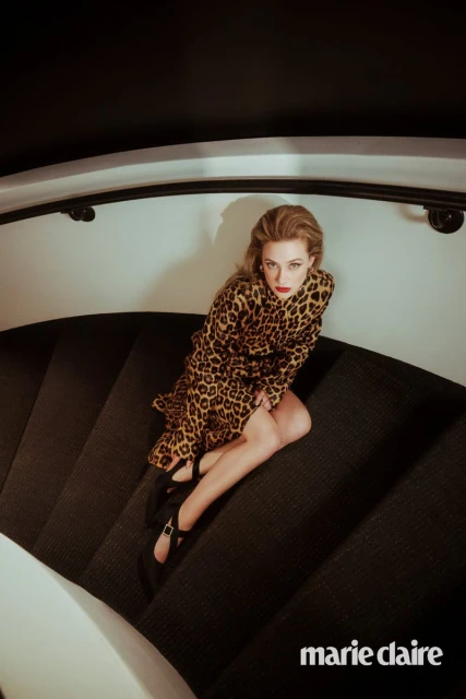 Blonde woman in leopard print dress sits on carpeted stairs, wearing Mary Jane shoes and red lipstick in a beauty fashion editorial.