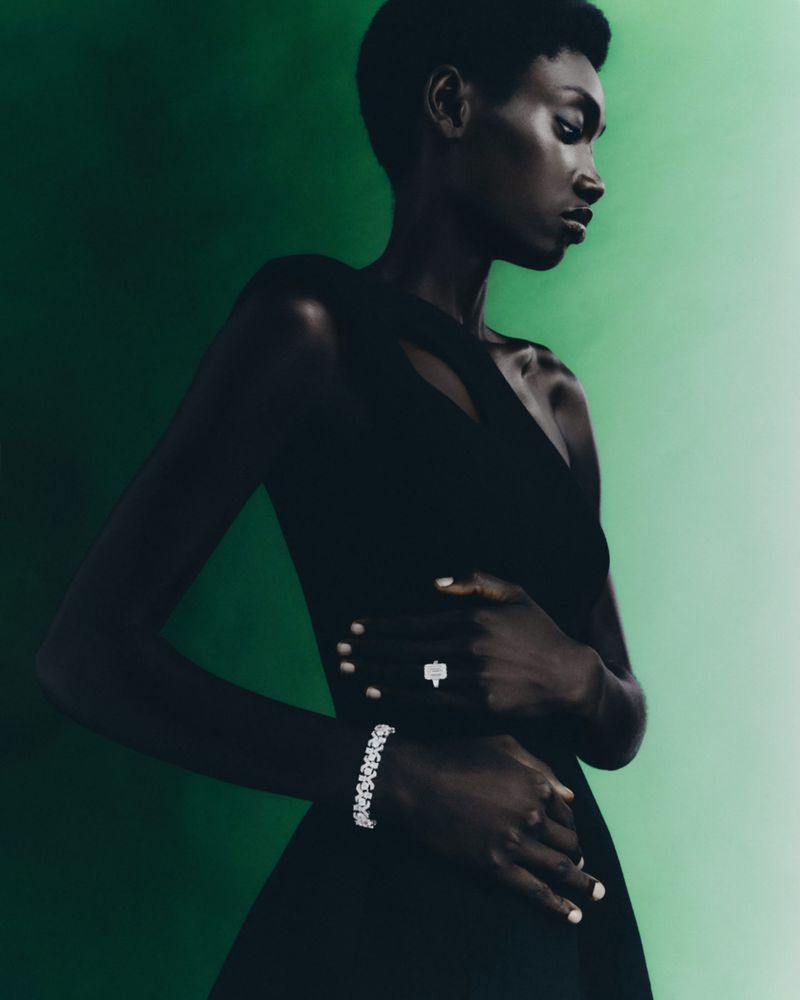 Elegant portrait of a Black woman in a black dress wearing diamond jewelry against a gradient green background, showcasing fashion and beauty.