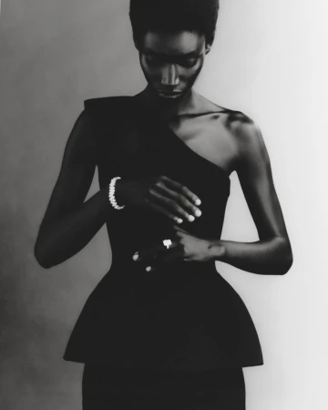 Portrait of a Black woman in a black one-shoulder dress, wearing jewelry, shot in a photo studio with a neutral background.