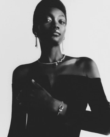 Black and white portrait of an elegant African-American woman wearing jewelry, a black dress, and standing in a photo studio.