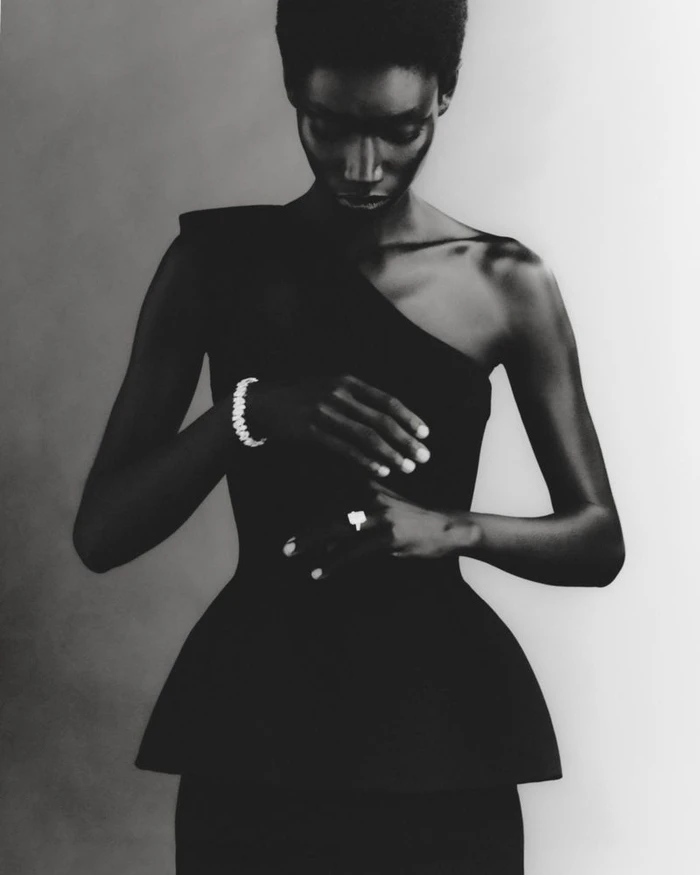 Black and white editorial portrait of a model wearing a dark fitted top with a flared peplum waist against a bright gradient background