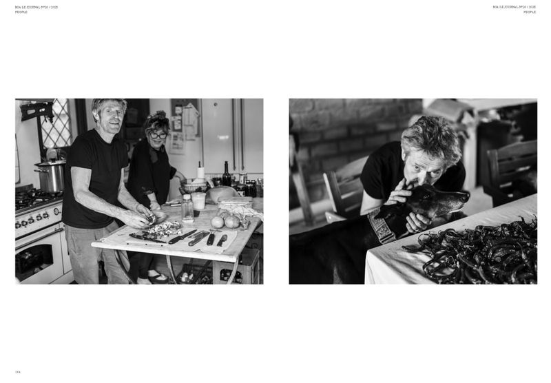 Black and white image shows a man and woman prepping food in a kitchen, while another man pets a dog on a table with peppers.