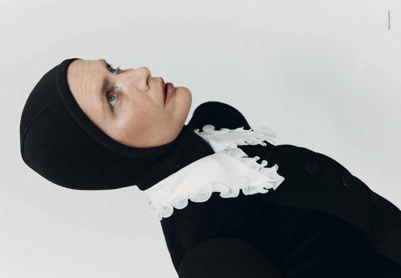 Elegant, close-up portrait of a woman in a black dress with a ruffled white collar and matching head covering against a white backdrop.