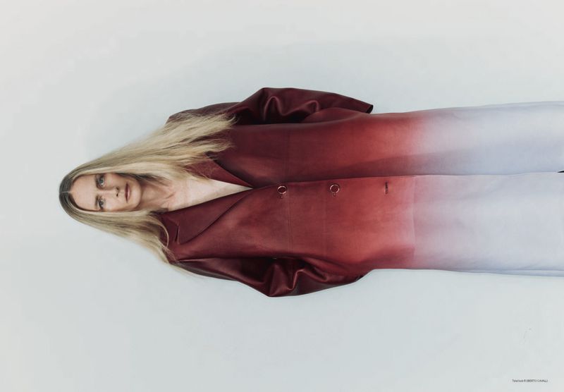 Fashion shot of a woman with long blonde hair wearing a gradient red and white jacket in front of a plain white backdrop.