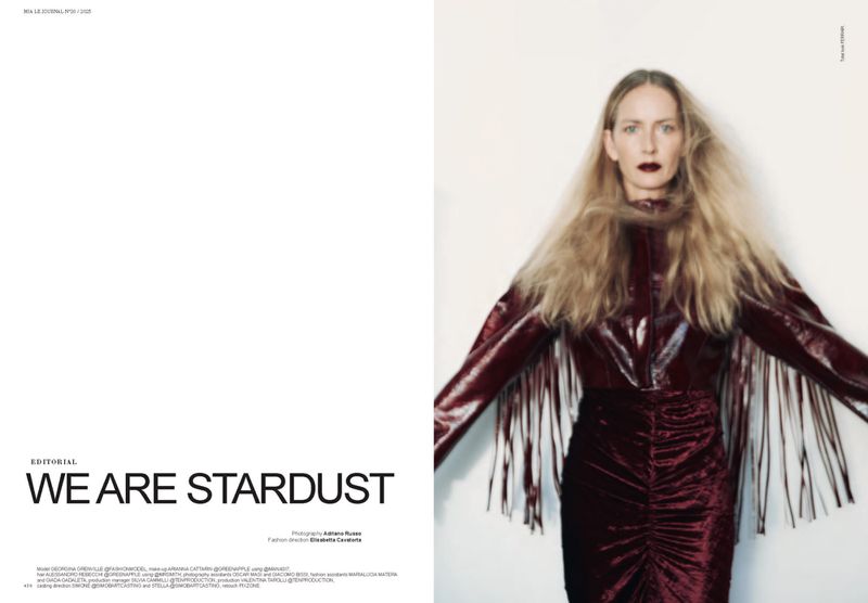 Fashion editorial shot of a blonde woman in a red dress with fringe sleeves, posing against a white background in a studio setting.