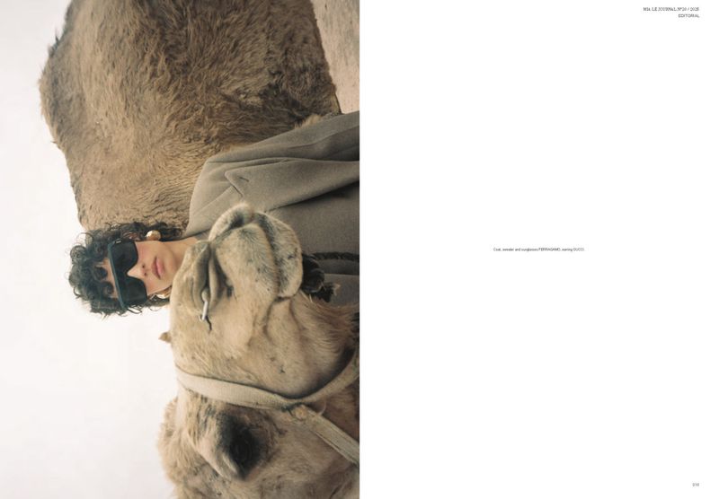 Editorial fashion shot features a woman in sunglasses and coat posing alongside a camel in a desert landscape, split-page magazine format.