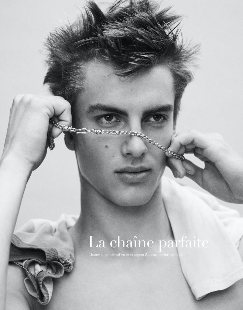 Close-up monochrome portrait of a young male model holding a silver chain across his face for Harper's Bazaar France Homme.
