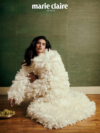 Editorial fashion shot of a woman wearing a voluminous white, feathery dress seated on the floor with a bowl of green grapes.