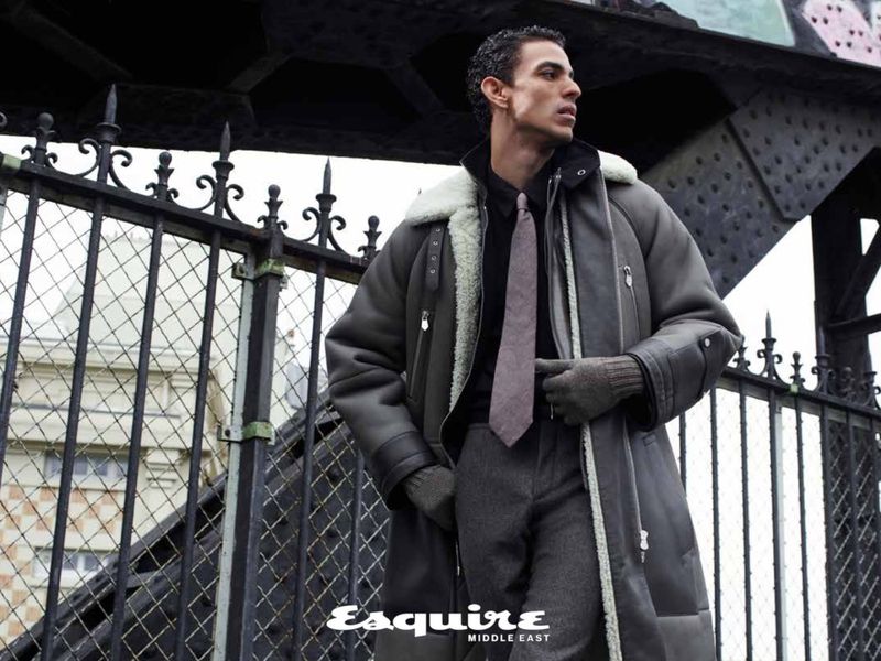Man in a grey coat and tie stands in front of a bridge, featuring Esquire Middle East magazine branding in the lower corner.