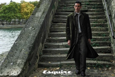 Man wearing a long green velvet coat and quilted trousers descending stone steps beside water for Esquire Middle East.