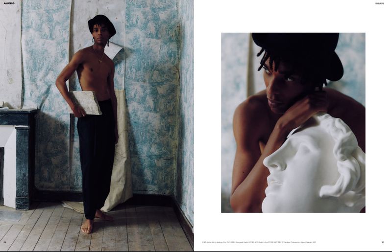 Indoor shot of a shirtless Black male model in baggy pants and a hat, holding a stone slab. Close up of the model with a sculpture.