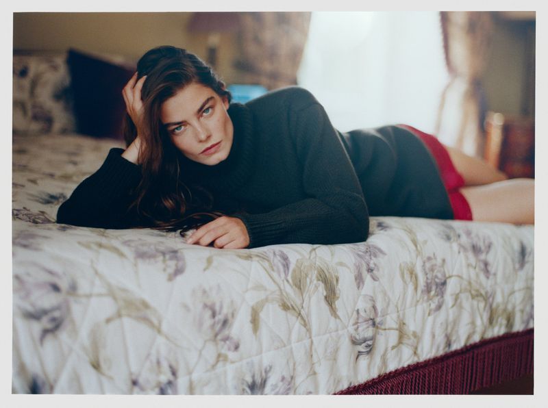 Model lying on a floral patterned bed wearing a dark turtleneck sweater for Vogue Netherlands Scotland Yarn editorial.