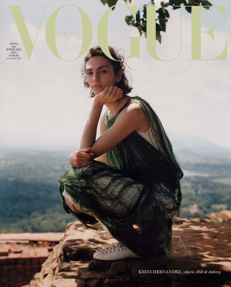 Vogue Polska cover with a young woman in a green dress crouching on a rocky surface, with a scenic landscape in the background.