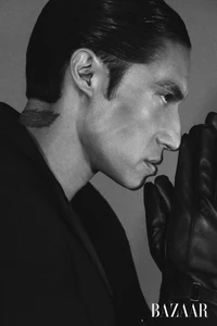 Profile portrait of a man in black leather gloves touching his face against a solid grey background for Harper's Bazaar China.