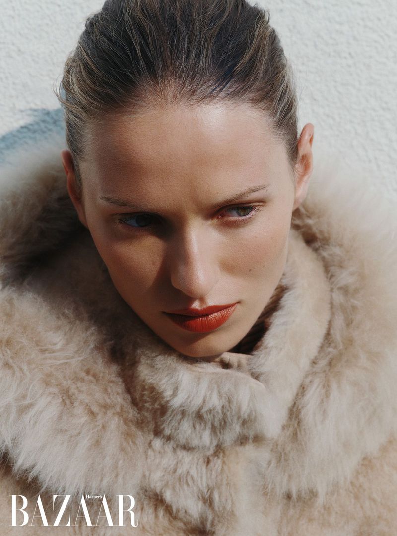 Close-up portrait of a woman wearing a fluffy textured coat against a textured neutral background for Harper's Bazaar UK.