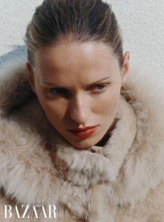 Close-up portrait of a woman wearing a fluffy textured coat against a textured neutral background for Harper's Bazaar UK.