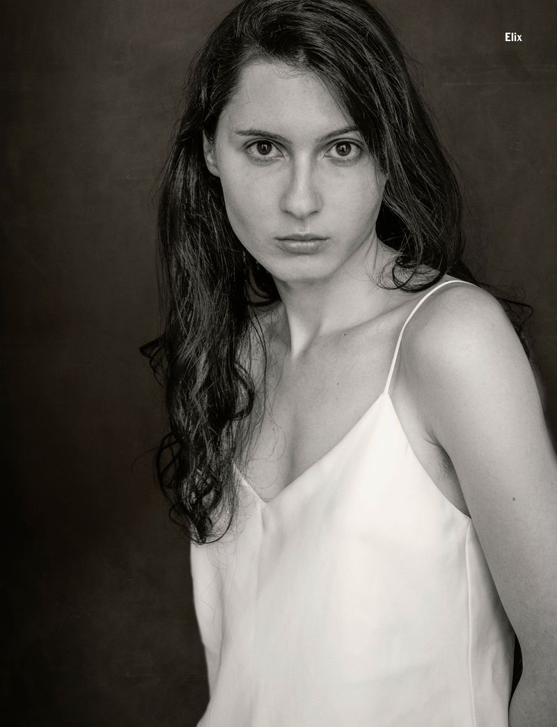 Monochrome portrait of a woman wearing a white slip top against a dark background, photographed by Derek Ridgers.