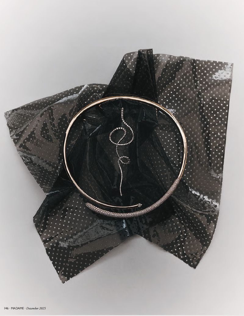 Still life shot of a gold choker necklace with a diamond pendant and detailing, presented on a shiny, patterned black fabric.