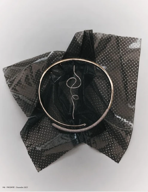 Still life shot of a gold choker necklace with a diamond pendant and detailing, presented on a shiny, patterned black fabric.