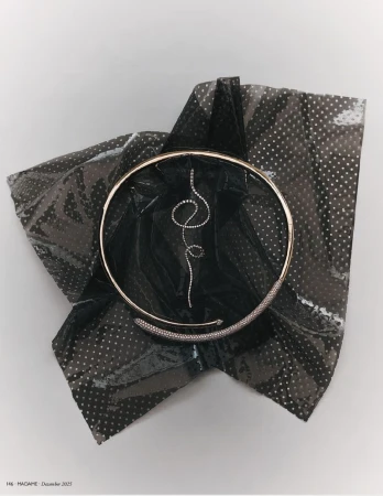 Still life shot of a gold choker necklace with a diamond pendant and detailing, presented on a shiny, patterned black fabric.