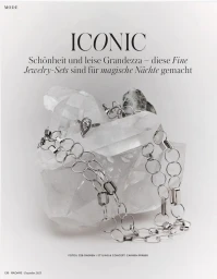 Silver chain necklace and pear-shaped diamond ring draped over a raw clear quartz crystal on a white editorial background.