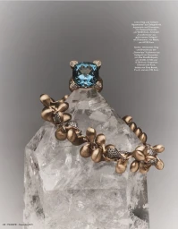 Gold and blue gemstone ring and sculpted gold bracelet displayed on a clear raw quartz crystal against a soft grey background.