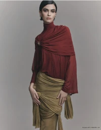 Model wearing a draped crimson turtleneck top and olive skirt against a plain grey background