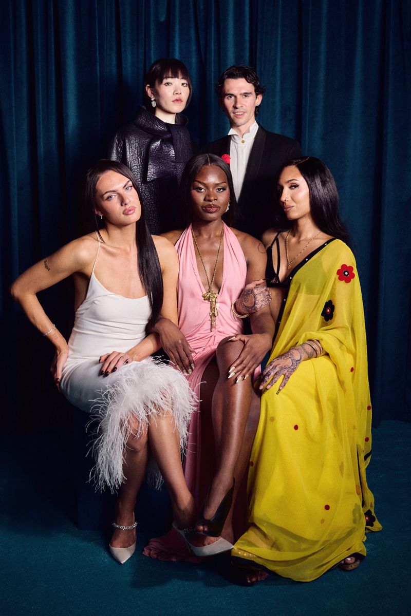 Group portrait of five diverse adults in formalwear against a dark teal curtain backdrop; elegant style, bright studio lighting.
