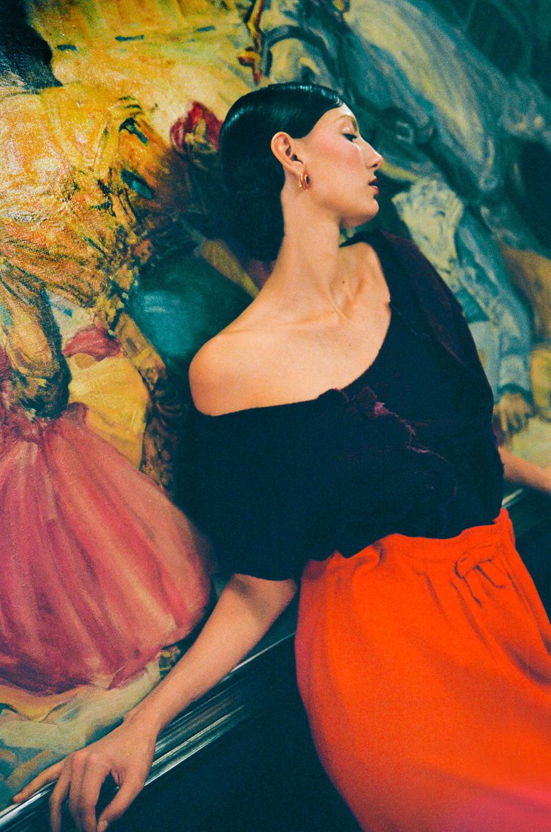 Adult woman poses in black top and orange skirt against abstract art background in portrait studio fashion photograph.