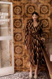 Model Cynthia Arrebola wearing a brown chevron belted coat standing beside a counter against an ornate patterned tiled wall.