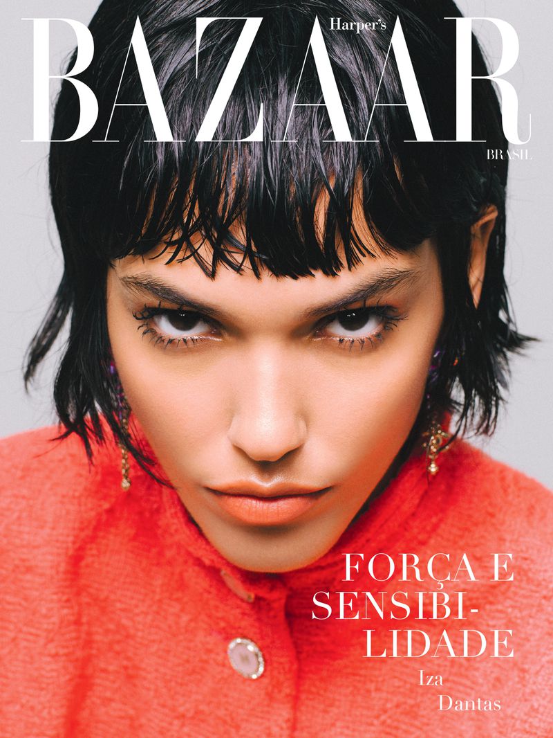 Close-up of a woman with short black hair and a coral tweed jacket against a grey background, as seen on a BAZAAR magazine cover.