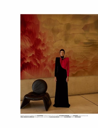 Woman in elegant black and red dress posing in a studio with modern chair and artistic background, fashion photography.