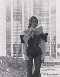 Model Karolina Capkova posing in a bow blouse and textured structured top against a modern glass skyscraper background.
