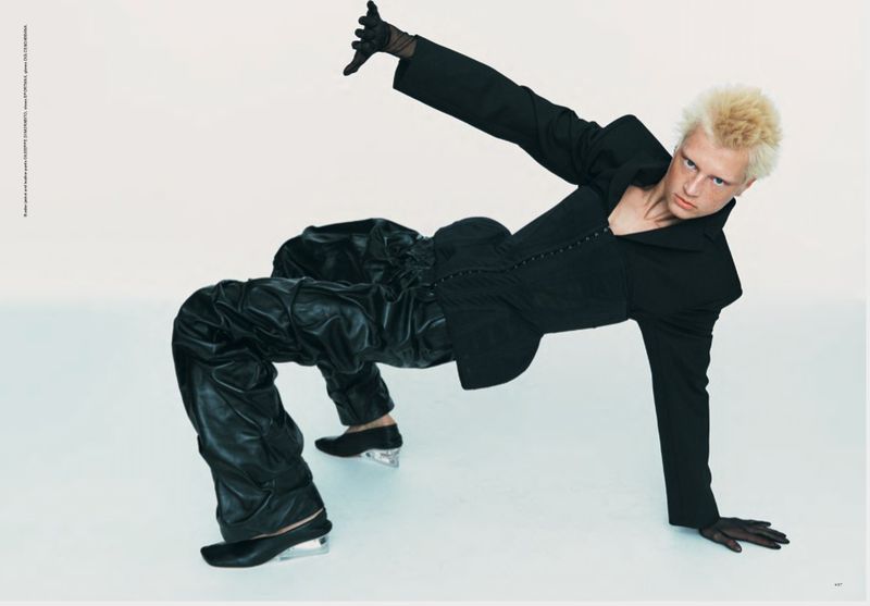 Fashionable adult poses in artistic studio shot with edgy black suit and innovative translucent heel shoes on white seamless backdrop.