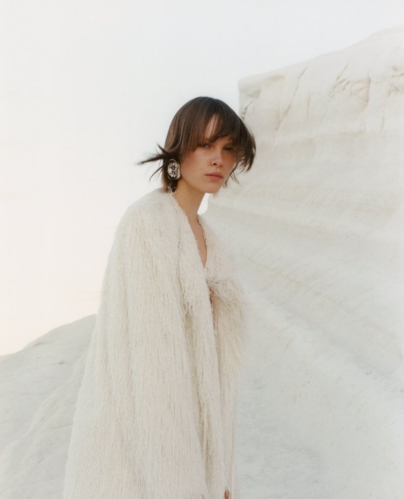 Model Thea Almqvist wearing a textured white coat against white rock formations for Beyond Noise