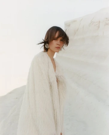 Model Thea Almqvist wearing a textured white coat against white rock formations for Beyond Noise