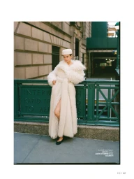 Model in a long white fluffy coat and pillbox hat standing by green railings for Elle Turkiye