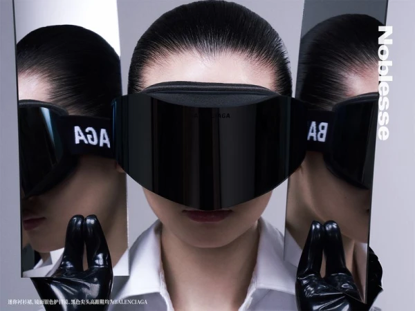 A woman poses in reflective goggles in a studio. Black gloves hold up mirrored panels with logo reflections. Fashion shot.