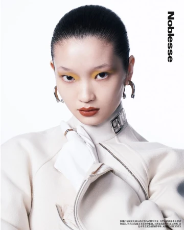 Close-up of an Asian woman with yellow eyeshadow and red lipstick wearing a white jacket and silver earrings in a studio shot.
