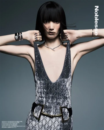 Model with dark bob hairstyle wearing a grey patterned dress and jewellery against a grey studio backdrop