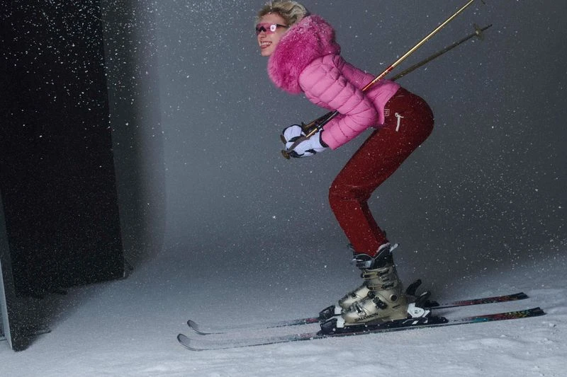 Stylish woman in pink jacket skiing downhill on snow with poles. Woman in ski apparel enjoying winter sport in an indoor snow setting.