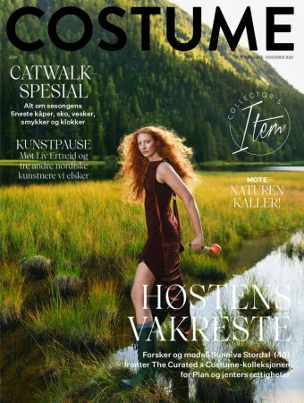 Magazine cover featuring a model in a brown dress walking through a grassy, marshy area with mountains and forest in the background.