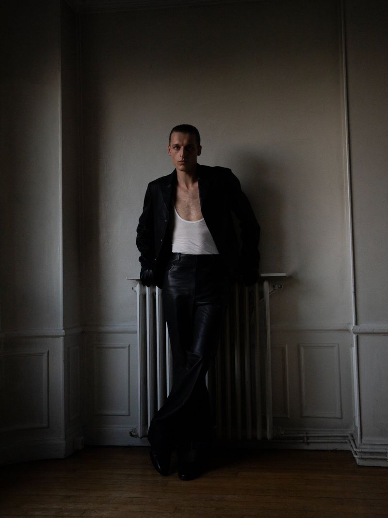 Model Colin Otto leaning against a radiator wearing a dark jacket and trousers for SSAW Magazine