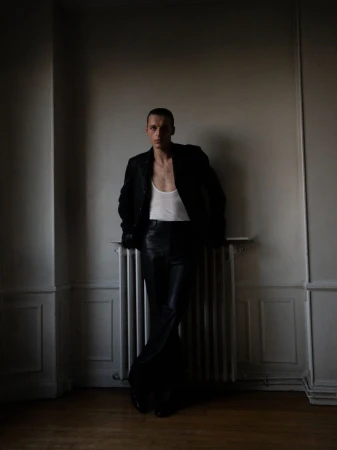 Model Colin Otto leaning against a radiator wearing a dark jacket and trousers for SSAW Magazine