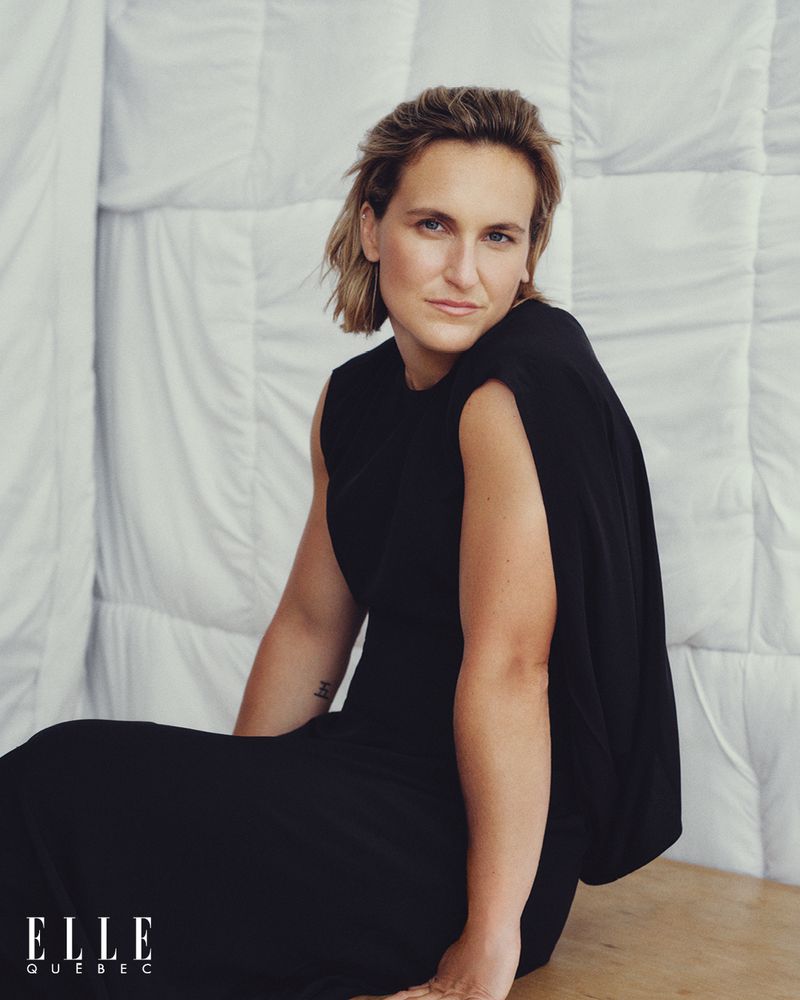 Blonde woman in black dress poses indoors against white quilted backdrop; portrait shot for Elle Quebec magazine cover.